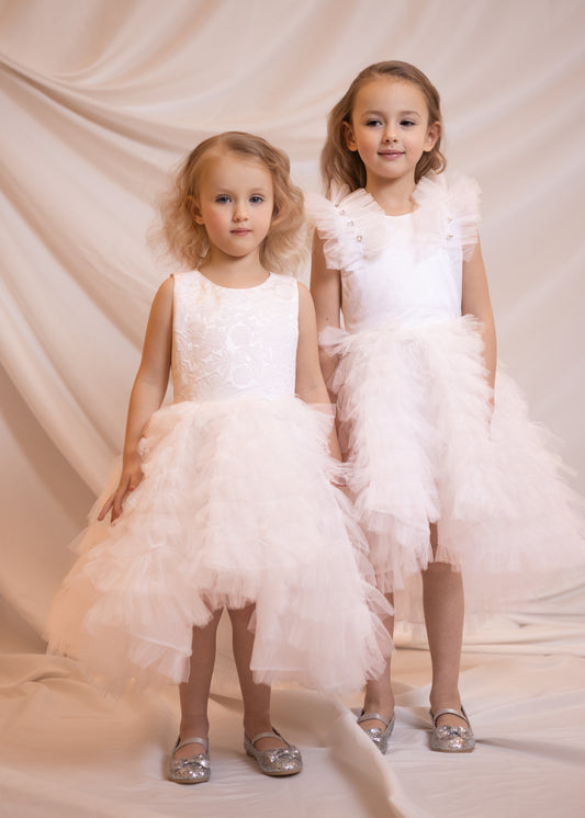 A luxurious display of high-end children's dresses in various shades of pink, blue, and purple, arranged elegantly in an upscale boutique setting.