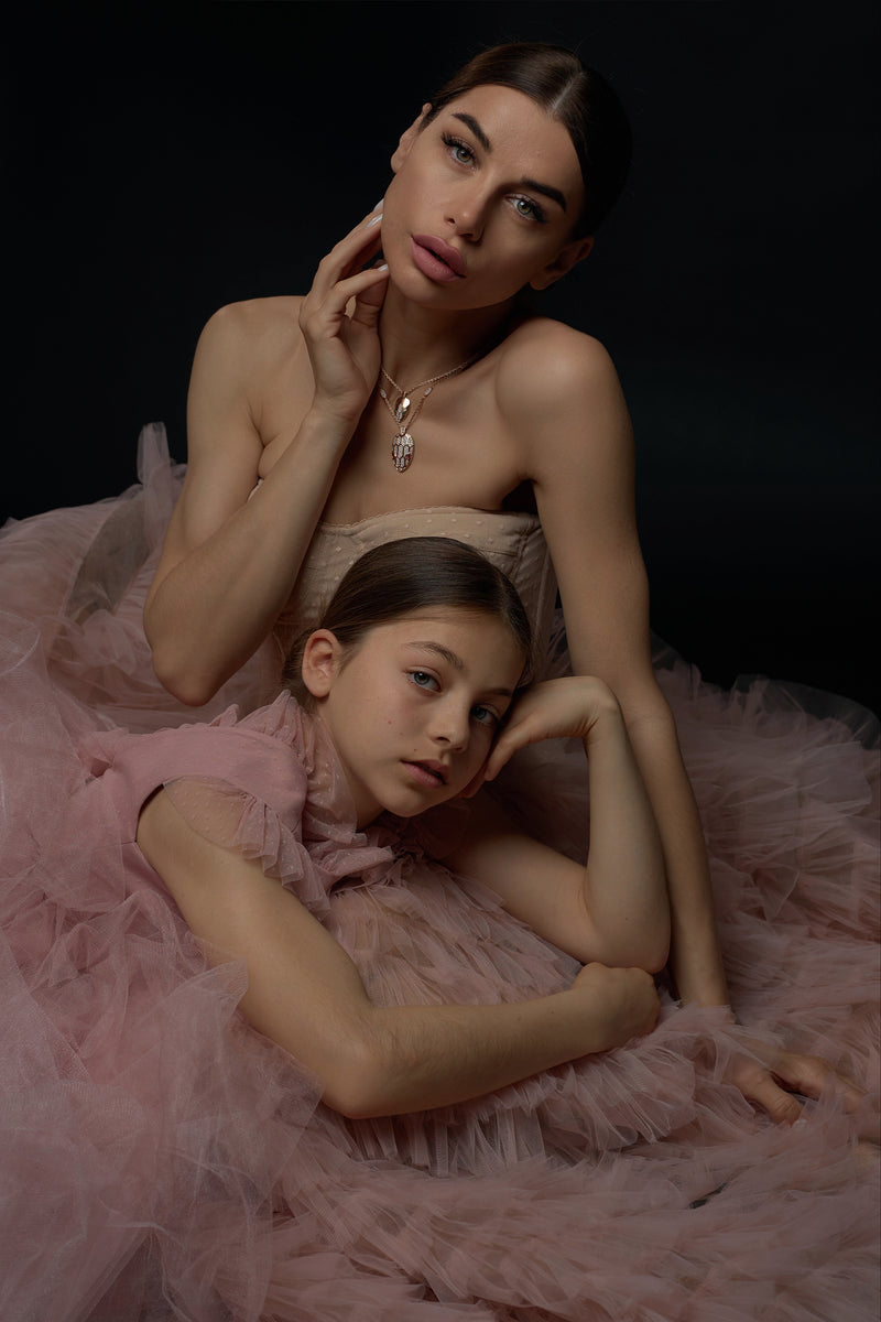 A mother and daughter in matching elegant dresses in a serene garden setting, surrounded by soft, romantic colors and blooming flowers.