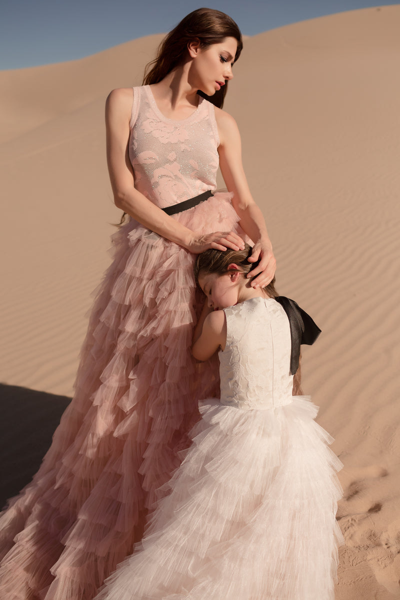 A mother and daughter in coordinated luxurious outfits in a romantic garden setting.