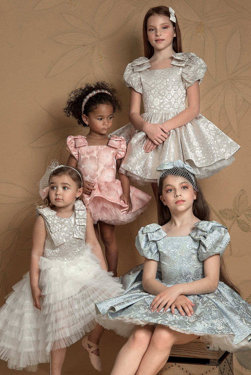 A group of 4 young girls, showcasing elegant flower girl dresses in white, pink, and baby blue, surrounded by soft lighting.