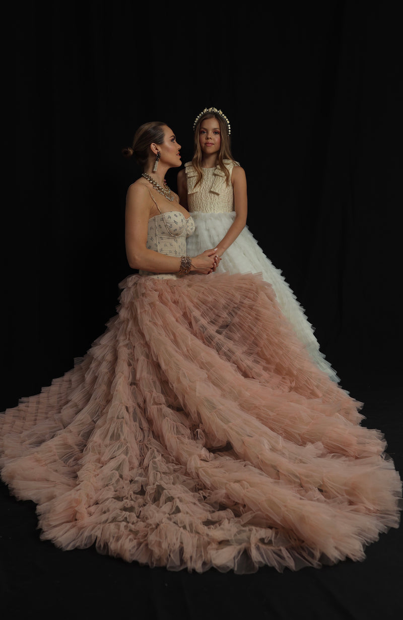 A mother and daughter in matching pastel gowns in a decorated garden.