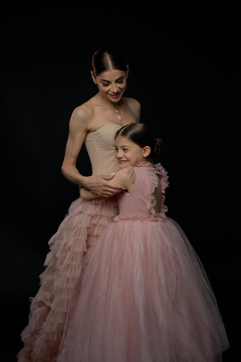 A mother and daughter elegantly dressed in matching couture dresses in a luxurious room.