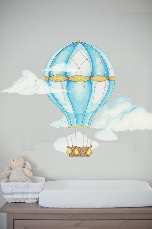 Blue hot air balloon wall decal with watercolor clouds above crib in baby nursery room