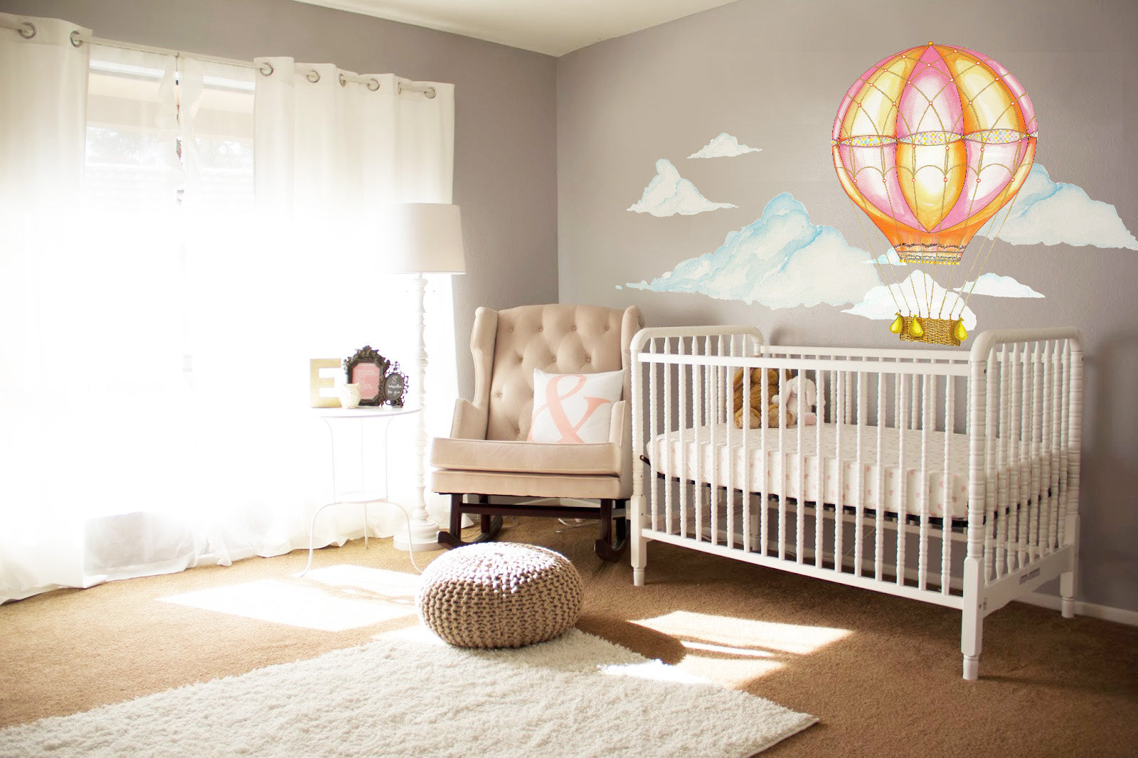 Pink hot air balloon wall decal with watercolor clouds above crib in baby nursery room