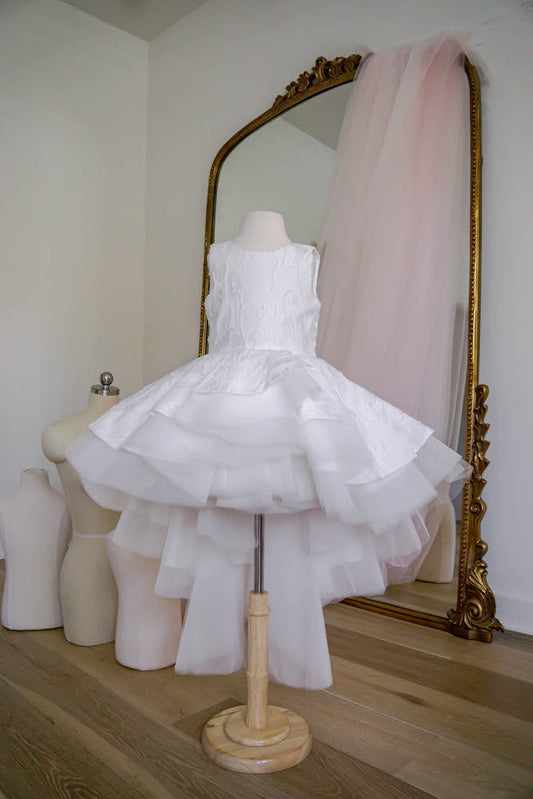White flower girl dress with embroidered bodice and layered high-low tulle skirt displayed on mannequin