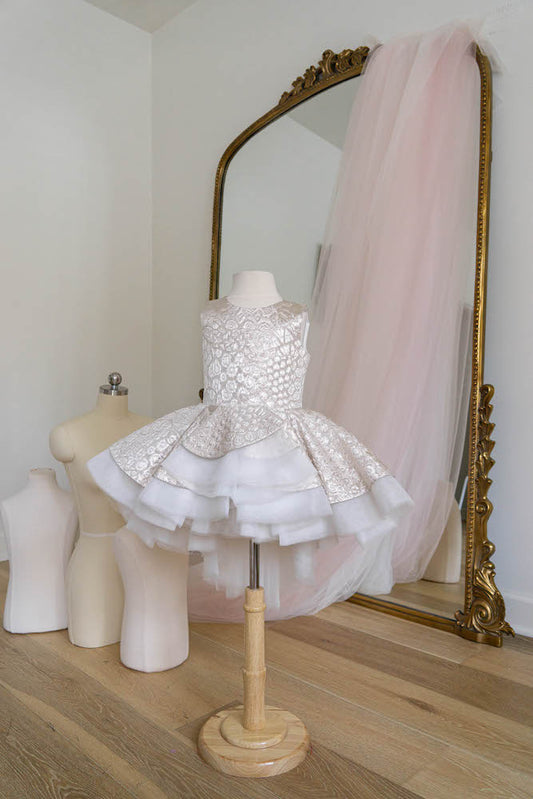 White and silver flower girl dress with embroidered bodice and layered high-low skirt displayed on mannequin